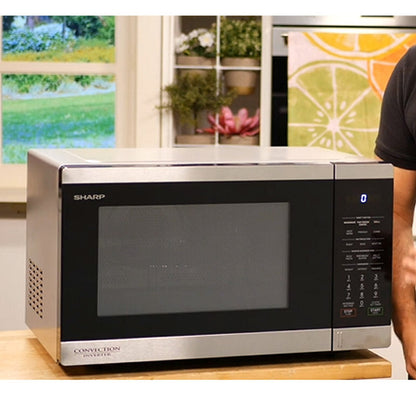 Sharp microwave oven on a kitchen counter with a window view of greenery.